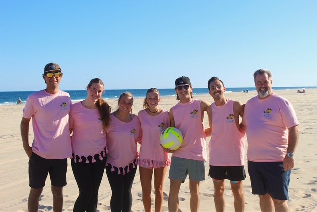 A team in pink shirts poses with the ball by the water
